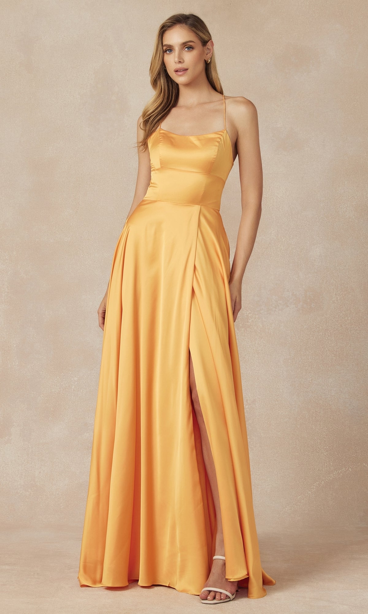 A woman stands against a beige background wearing the Strappy-Back Simple Long A-Line Prom Dress 278, a sleeveless yellow satin gown featuring a thigh-high slit.